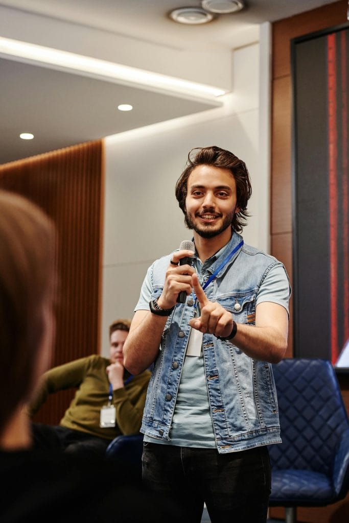 Life At Harjai Technologies 10 A confident speaker engaging with the audience during an indoor conference, using a microphone.