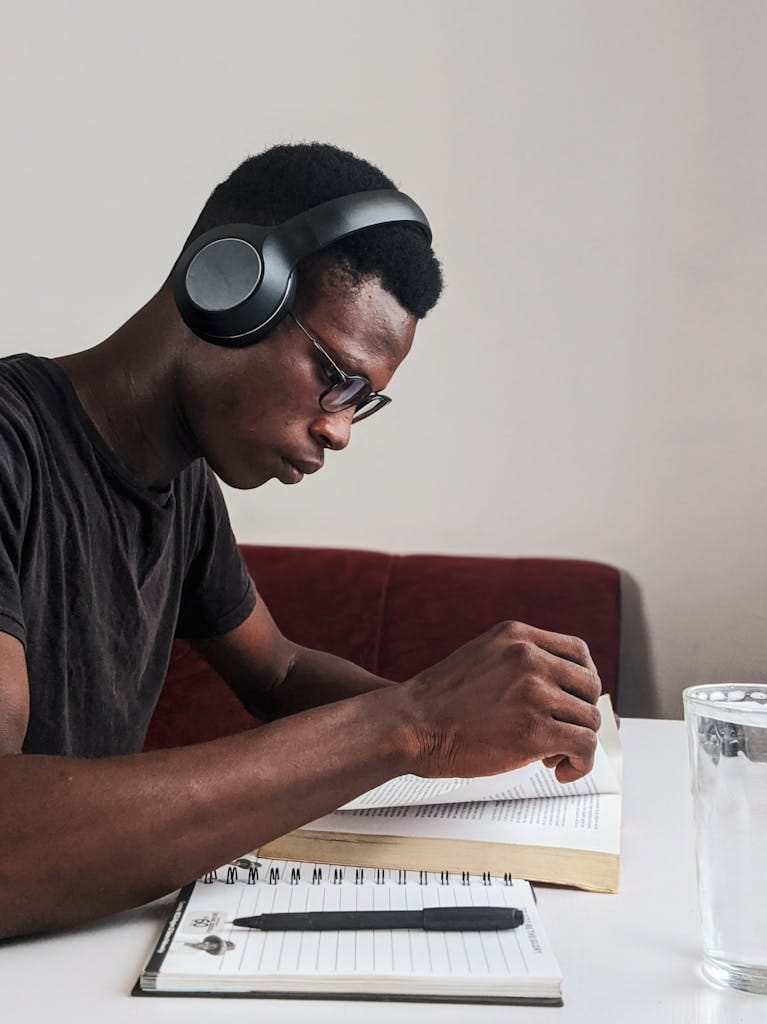 E-Learning 14 An adult man intensely studying with headphones, pen, and notebook at a desk indoors.