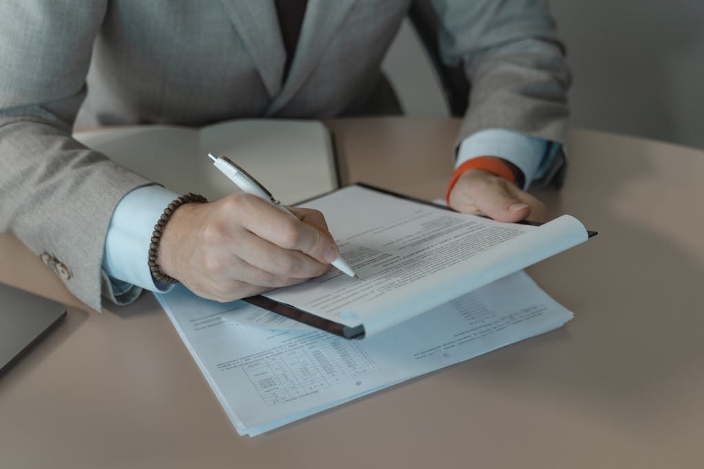 E-Learning 12 Close-up of business person signing documents at a desk with a pen.