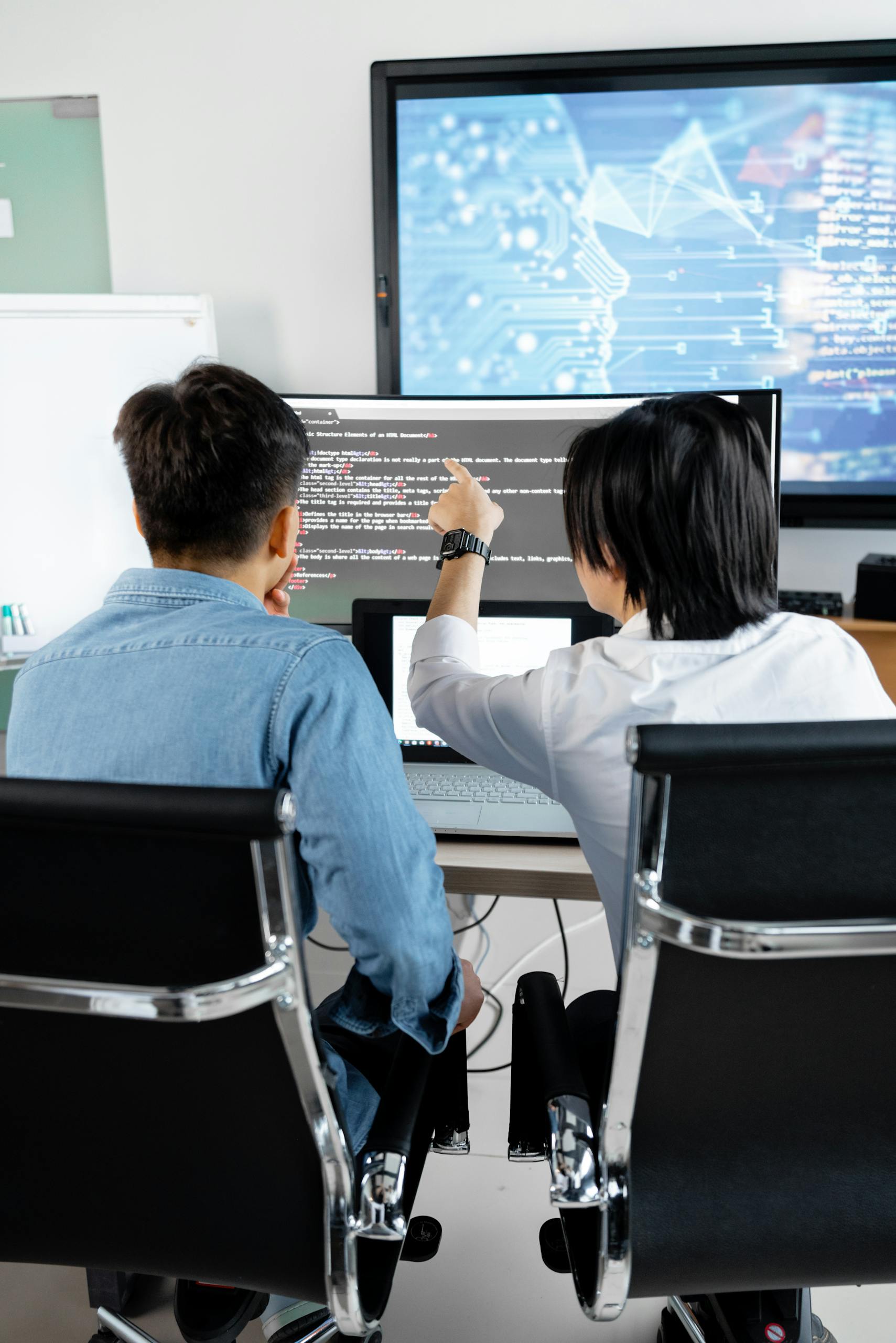 FMCG & FMEG 14 Two adults collaborating in an office, discussing code on a computer screen.