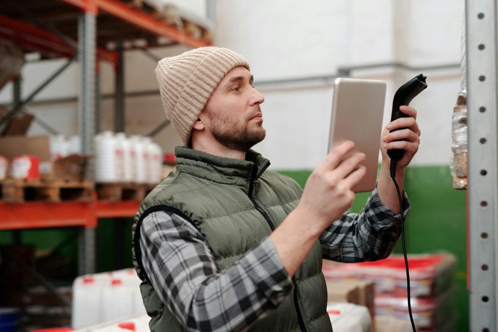 Retail & CPG 11 Man in beanie and vest using a scanner in a warehouse for inventory control.